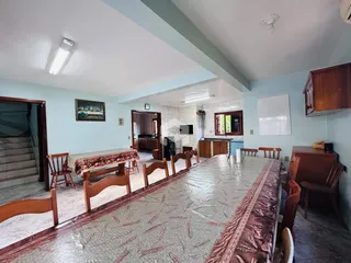 Imagem de uma sala de jantar com mesa longa e cadeiras de madeira.