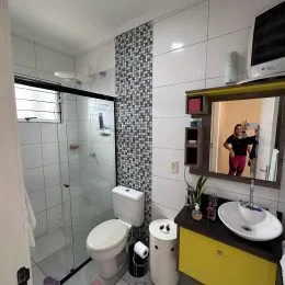 Banheiro com revestimento de azulejos brancos e box de vidro.