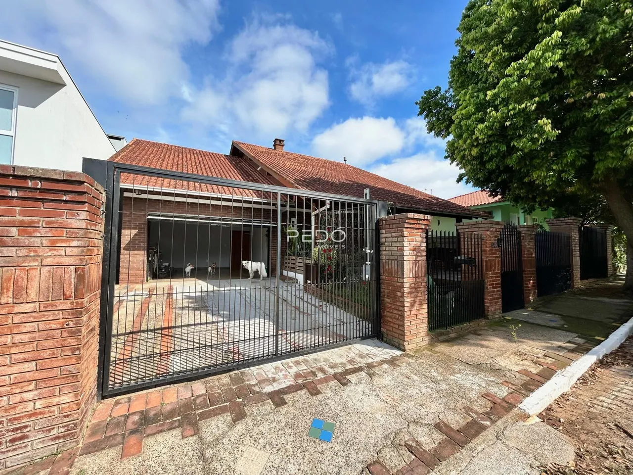 Fachada de uma residência com muro de tijolos e portão de ferro na entrada.