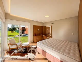 Quarto com cama grande, piso de madeira e acesso a uma área externa gramada.