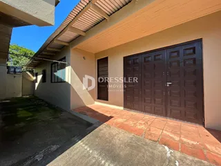 Vista da fachada de uma residência com área coberta e piso de tijolos vermelhos.