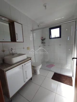 Banheiro com bancada branca e box de vidro transparente.