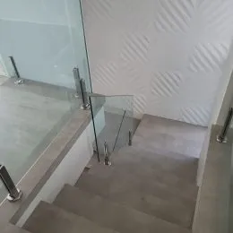 Foto de uma escadaria com guarda-corpo de vidro em um ambiente interno.