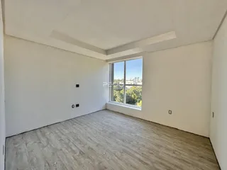 Sala de estar com piso de madeira clara e grande janela.