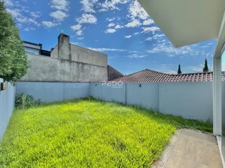 Vista externa do terreno com gramado e muro de vedação.
