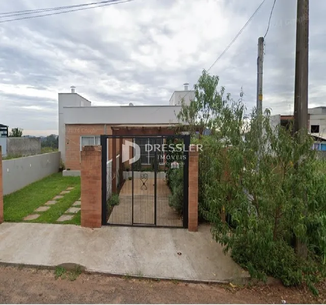 Fachada de uma propriedade com portão de ferro e vegetação ao redor.