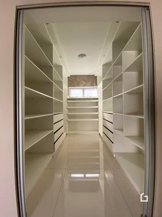Hall de corredor interno com estantes brancas e escadaria.