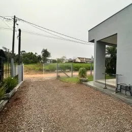Vista da entrada de uma propriedade com piso de cascalho e vegetação.