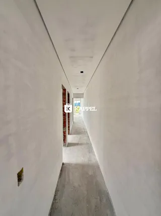 Corredor longo e estreito com paredes brancas e piso de concreto.