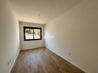 Ambiente interno de uma sala com piso de madeira clara e parede branca.