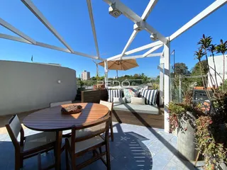 Vista de uma área externa com mesa e sofá sob uma estrutura de pérgola.