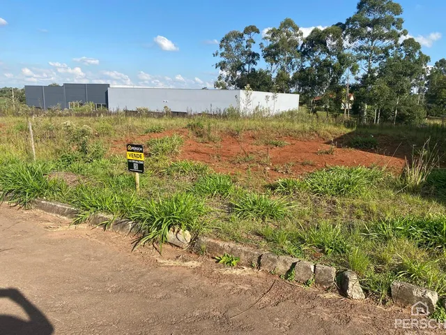Vista externa de um terreno com vegetação e um edifício moderno ao fundo.