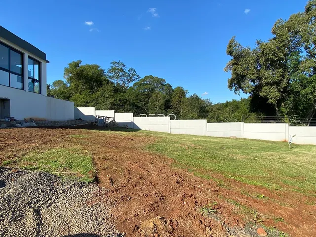 Vista externa de uma residência com terreno aberto e vegetação ao fundo.