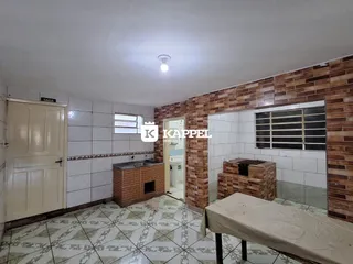 Foto interna de uma área de cozinha com piso de azulejos e parede de tijolos aparentes.