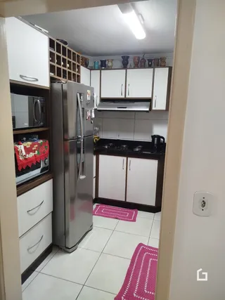 Vista interna de uma cozinha com armários brancos e eletrodomésticos de aço inoxidável.