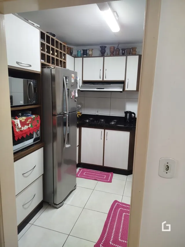 Vista interna de uma cozinha com armários brancos e eletrodomésticos de aço inoxidável.