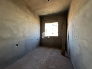 Interior de um espaço com paredes de concreto aparente e piso cru.