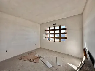 Ambiente interno de uma sala com piso de concreto cru e janela de madeira.
