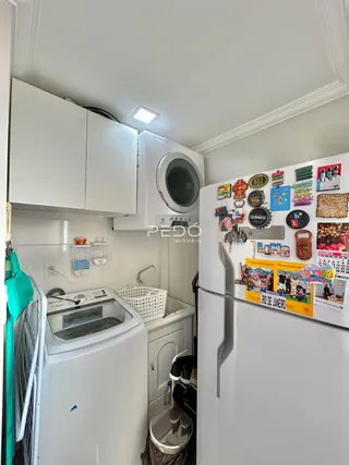 Interior de uma área de serviço com máquina de lavar e geladeira branca.