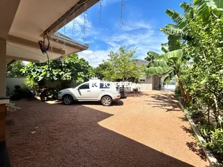 Vista externa do terreno com cascalho e vegetação tropical.
