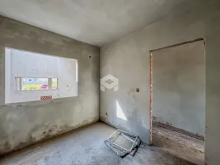 Foto de um cômodo interno com paredes de concreto cru e uma abertura de porta.
