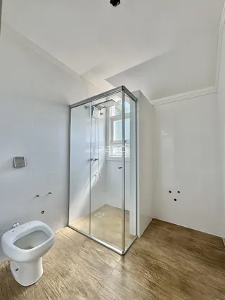 Banheiro moderno com box de vidro e piso de madeira clara.