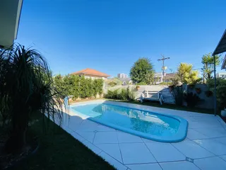 Piscina externa com jardim e vegetação ao redor.