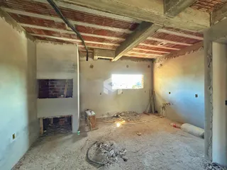 Interior de uma sala em construção com teto exposto e paredes em fase de acabamento.