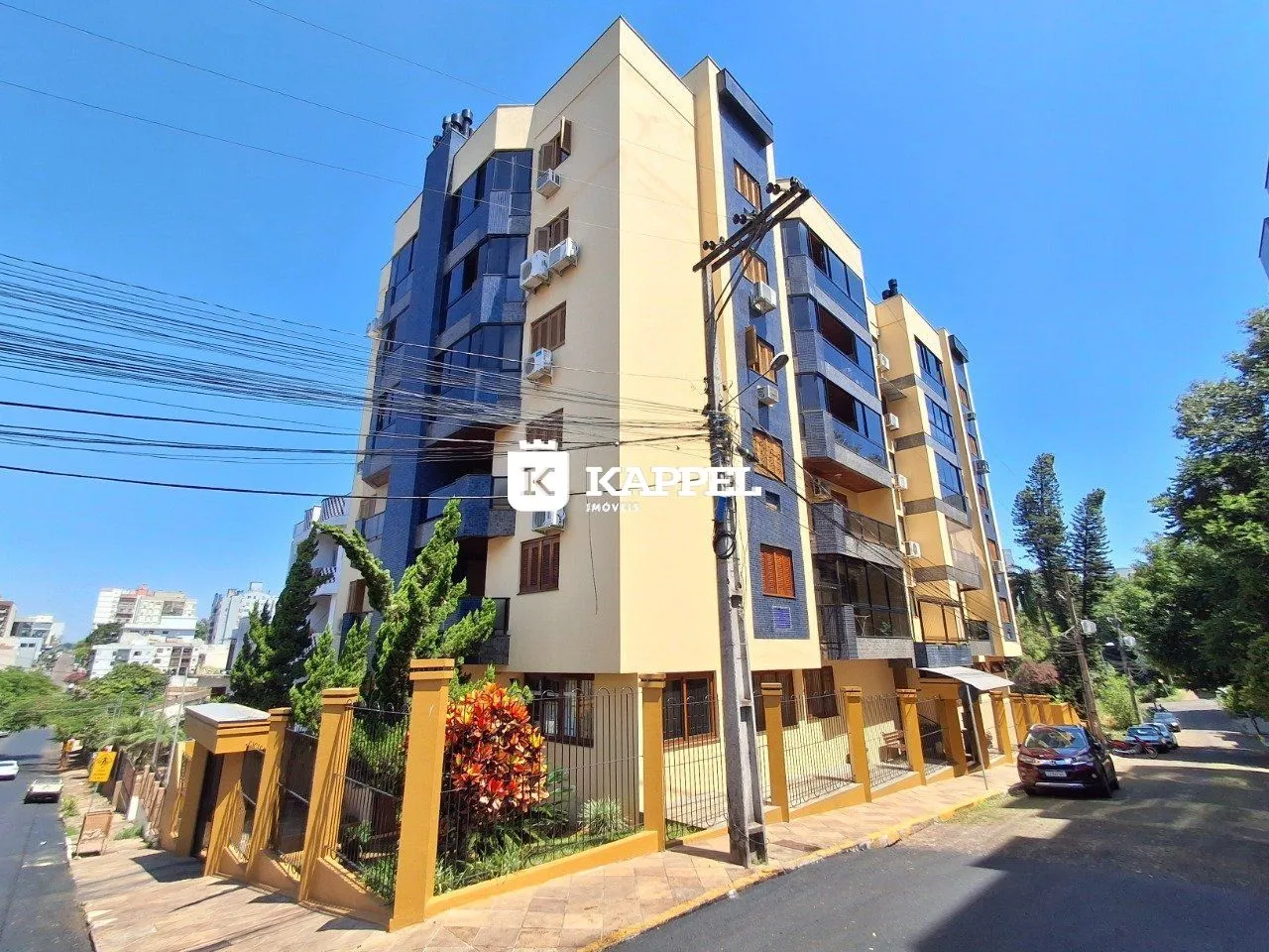 Fachada de um prédio residencial em Lajeado, Brasil, com jardim e estacionamento na rua.