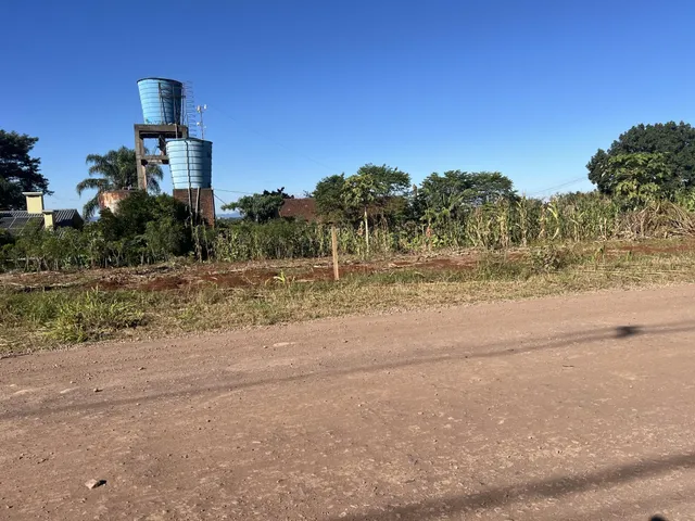 Vista externa da propriedade mostrando vegetação e estruturas industriais ao fundo sob um céu azul.