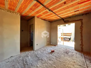 Foto de um cômodo interno em construção com paredes e teto expostos.