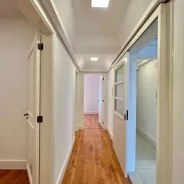 Corredor interno com piso de madeira e paredes brancas.