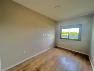 Ambiente interno de uma sala com piso de madeira clara e janela.