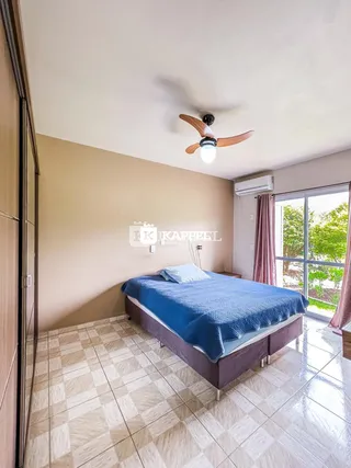 Quarto com cama azul e janela com vista para a vegetação externa.