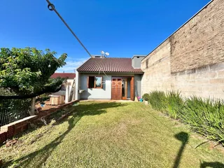 Vista externa de uma residência com um quintal gramado e muro de alvenaria.