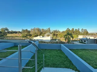 Vista externa de um jardim cercado com muro baixo e grade metálica.