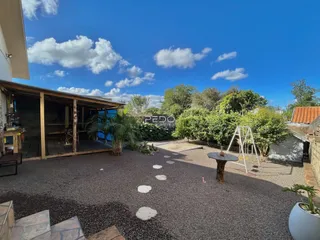 Vista externa de um quintal com vegetação e piso de cascalho.
