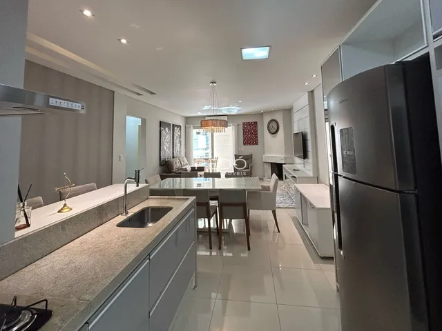 Vista de uma cozinha moderna com ilha e área de jantar em um apartamento.