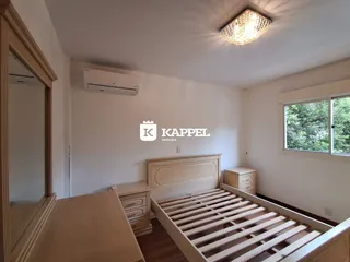 Quarto com cama de madeira e janela, apresentando paredes brancas e piso de madeira.