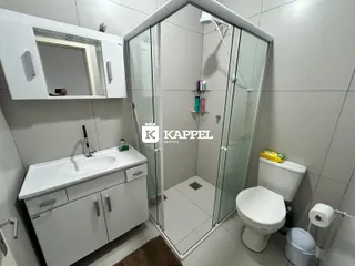 Foto interna de um banheiro com bancada branca e box de vidro.