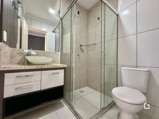Interior de um banheiro com box de vidro e louças brancas.