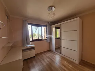 A sala apresenta piso de madeira e uma grande janela com cortinas.