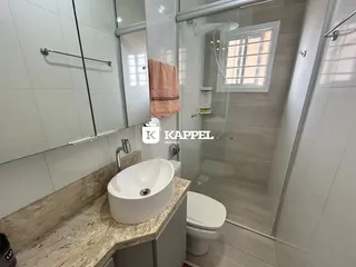 Banheiro com bancada de mármore e box de vidro transparente.