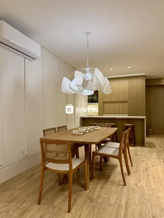 Uma sala de jantar com mesa de madeira e luminária pendente em um ambiente claro.
