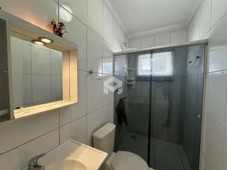 Banheiro com revestimento branco e box de vidro transparente.