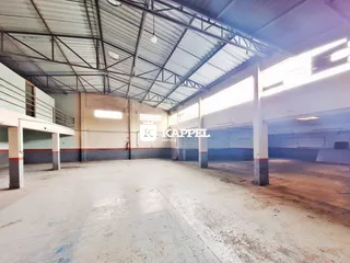 Vista interna de um espaço industrial com estrutura metálica e piso de concreto.
