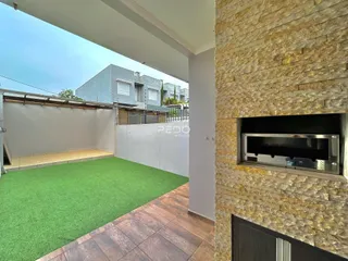 Vista de uma área externa com piso de grama artificial e parede de pedra em uma residência.