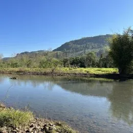 Vista de um rio e colinas verdes sob um céu azul claro.