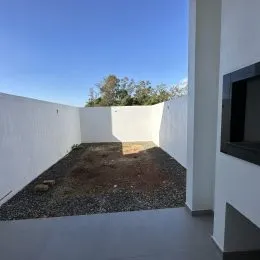 Vista externa de um pátio com piso de concreto e muro branco.