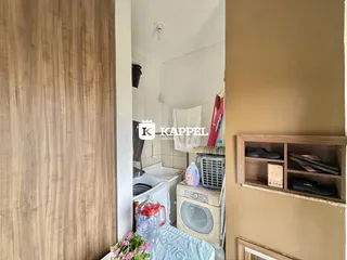 Foto interna de um banheiro com máquina de lavar e prateleira de madeira.